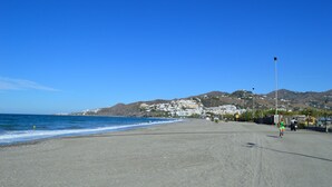 A beach with a clear sky, a sandy shore, and buildings in the background. - Villa Caritas Punta Lara by Casasol (Nerja)
