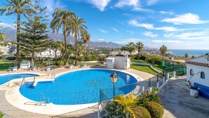 A swimming pool with a curved edge, surrounded by palm trees and a view of the sea and mountains in the background. - Villa Caritas Punta Lara by Casasol (Nerja)