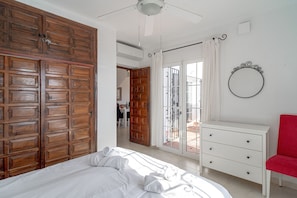Une chambre à coucher avec un grand lit, une armoire en bois, une commode blanche et un fauteuil rouge.