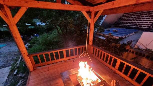 Um deck externo com lareira no centro, rodeado por guarda-corpos de madeira e uma mesa de metal.