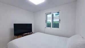 Quarto com cama, televisão em suporte, janela e luminária no teto.