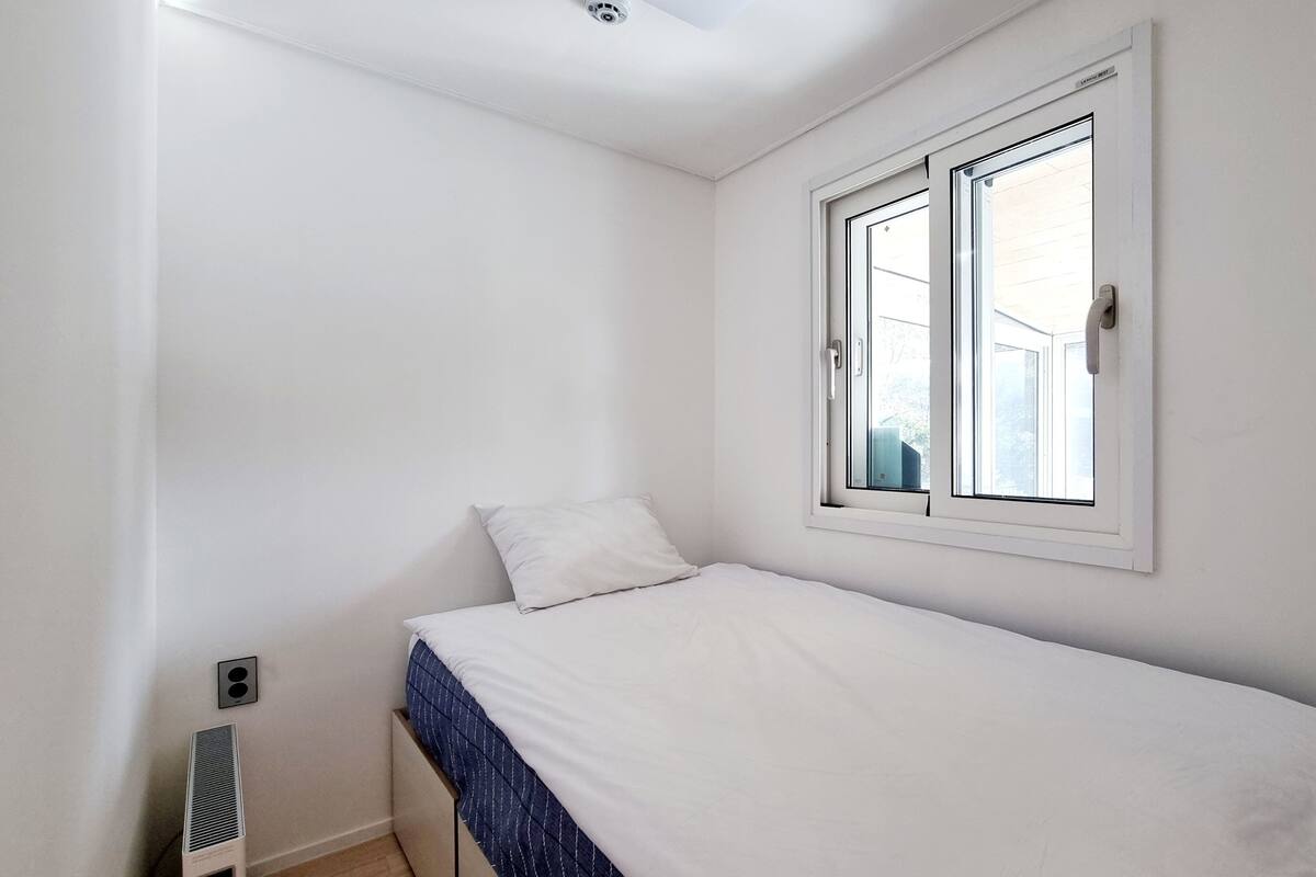 Een kleine eenpersoonskamer met witte muren, een raam met uitzicht en een radiator aan de muur.