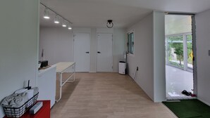 Um corredor com uma mesa, uma cesta de toalhas, um radiador branco e uma janela com vista para o verde.