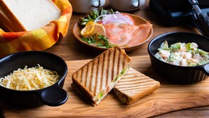 A wooden table with a sandwich, a bowl of salad, a bowl of shredded cheese, and a portable griddle. - From P (Hakuba)