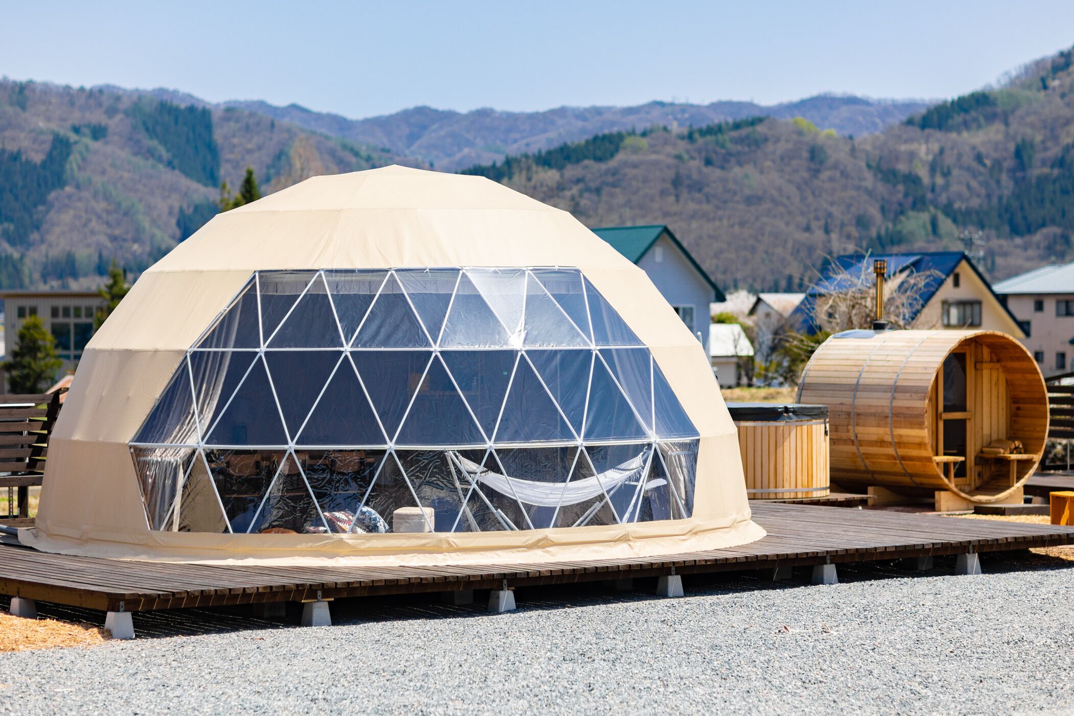 A geodesic dome structure with a transparent roof, a wooden deck, and a sauna.