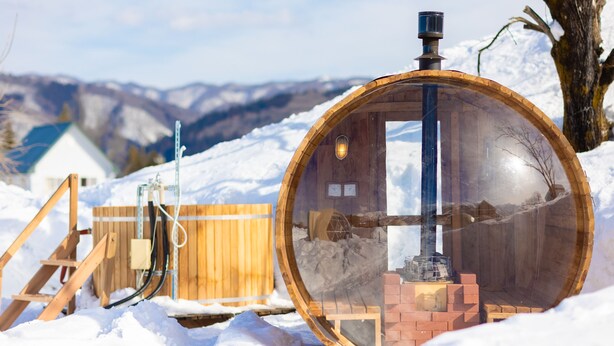 A transparent wooden structure with a chimney, surrounded by snow, and a wooden fence in the background. - From P (Hakuba)