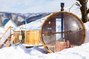 A transparent wooden structure with a chimney, surrounded by snow, and a wooden fence in the background. - From P (Hakuba)