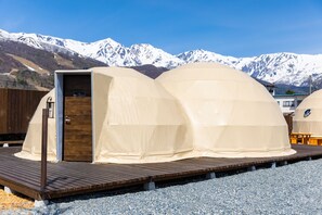 A set of dome-shaped tents with a wooden deck in front, set against a backdrop of snow-capped mountains. - From P (Hakuba)