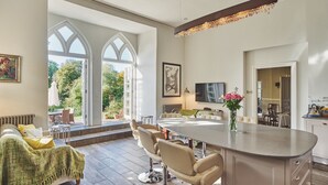 A spacious living area with a large dining table, comfortable seating, and a view of the outdoors through large windows.