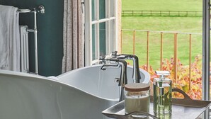 A bathroom with a bathtub, a sink, and a window overlooking a green field.
