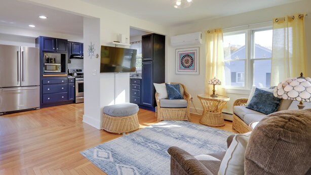 A modern kitchen with stainless steel appliances, a dining area with wicker furniture, and a living room with a large window. - Cozy Historic Wakefield Home Close to Beaches (South Kingstown)