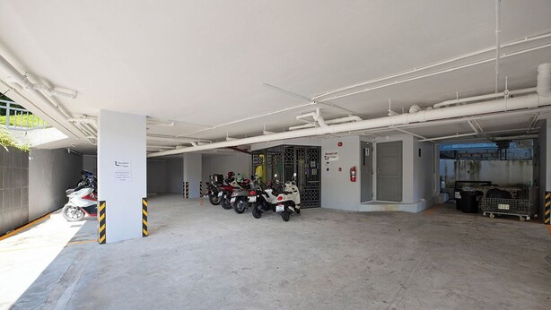 A covered parking area with concrete flooring, several motorcycles, and a fire extinguisher. - Icheck Inn Darisa Patong (Patong)