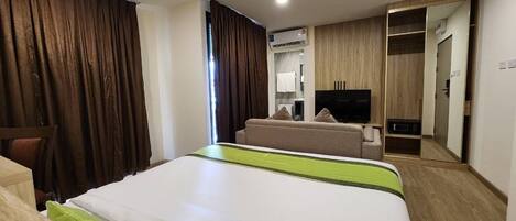 A hotel room with a bed, a sofa, a TV, an air conditioning unit, and a wardrobe.