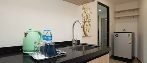 A modern kitchen with a black countertop, stainless steel sink, and a green kettle. There are two bottles of water and a tray with glasses on the counter.