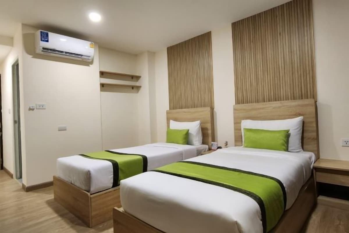 A hotel room with two beds, each with a wooden headboard and green accents.