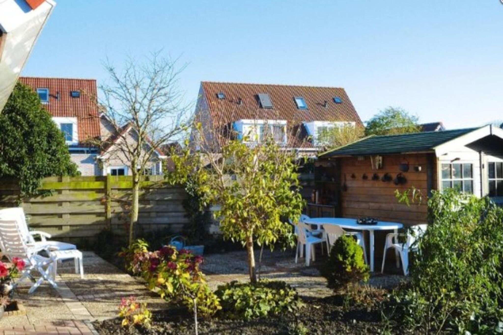 Een tuin met een houten tafel en stoelen, een kleine boom en een pad van bakstenen.