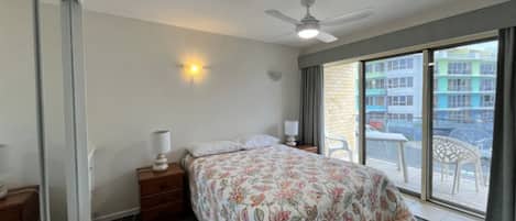A bedroom with a bed, bedside tables, a ceiling fan, and a view of the outside.