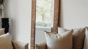 A living room with a large mirror, two beige sofas, a coffee table with decorative items, and a window with a view of greenery. - THE BAY. Effortless family fun. Pet friendly. (Nelson Bay)