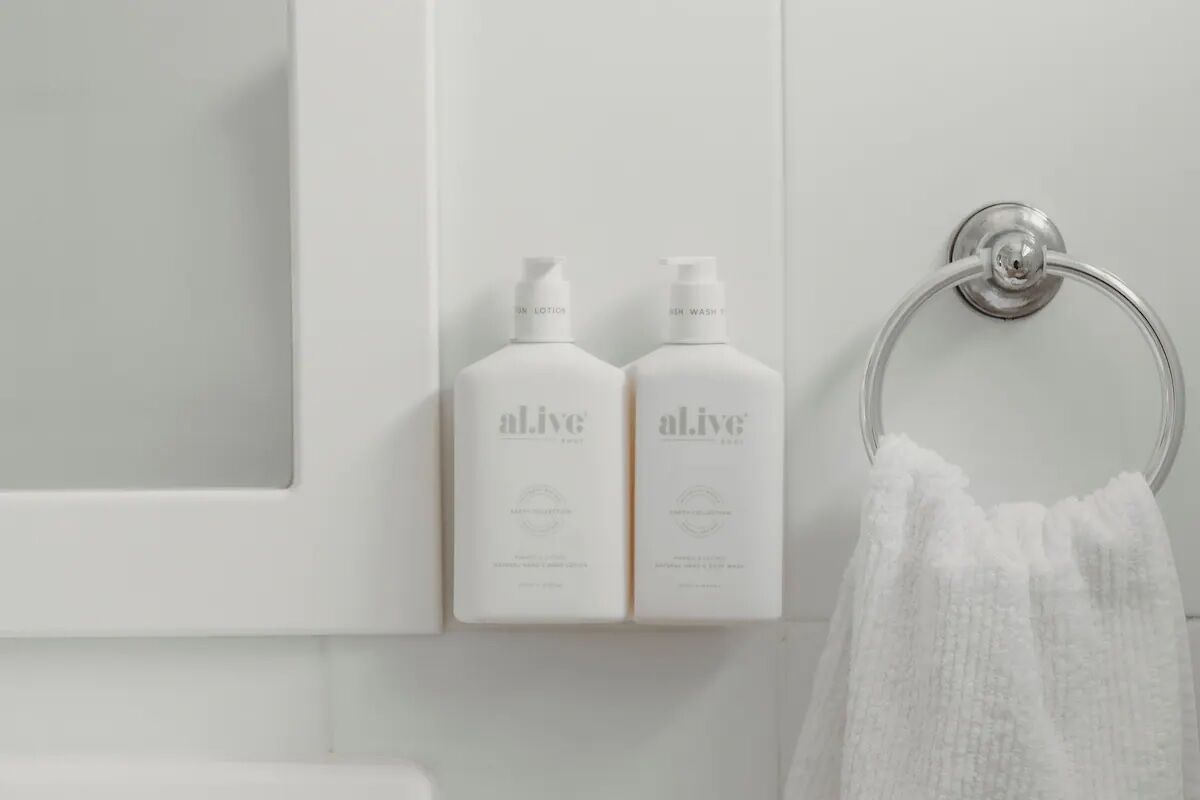 Een badkamer met twee flessen 'alive' zeep en een handdoekhouder met een witte handdoek.