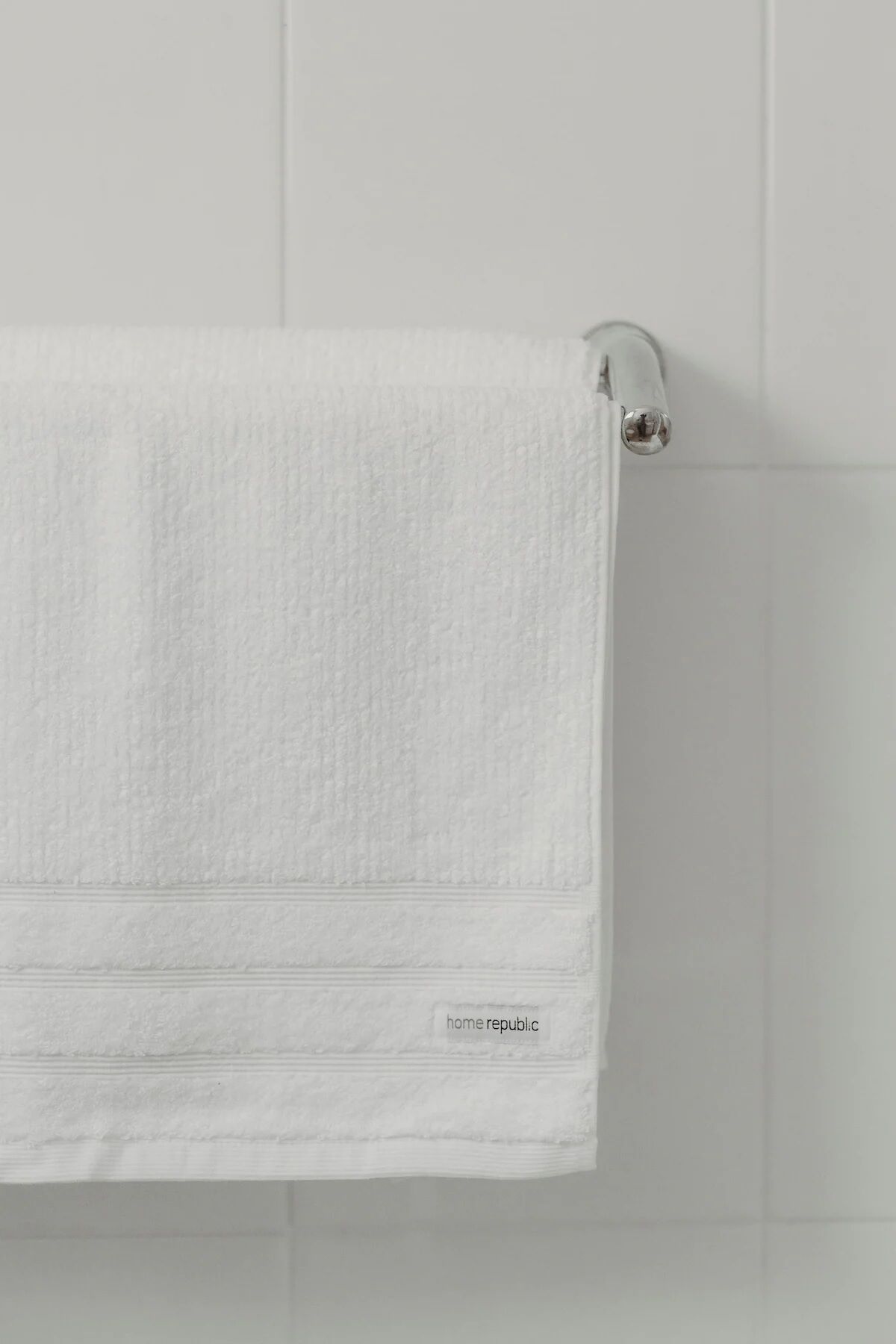 A white towel hanging on a white towel rack against a white tiled wall.