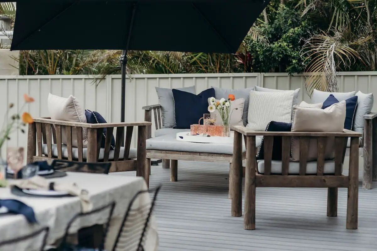 Un espace extérieur aménagé en terrasse, avec des meubles en bois, notamment un canapé et des fauteuils, placé sous un grand parasol.