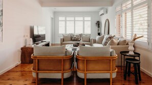 A living room with a sofa, two armchairs, a coffee table, a TV, and a window with blinds. - THE BAY. Effortless family fun. Pet friendly. (Nelson Bay)