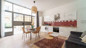 Una cocina moderna con armarios blancos, salpicadero con motivo de hering y una zona de comedor con sillas de mimbre y una mesa.