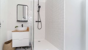 Un baño moderno con lavamanos, espejo y ducha blancos.