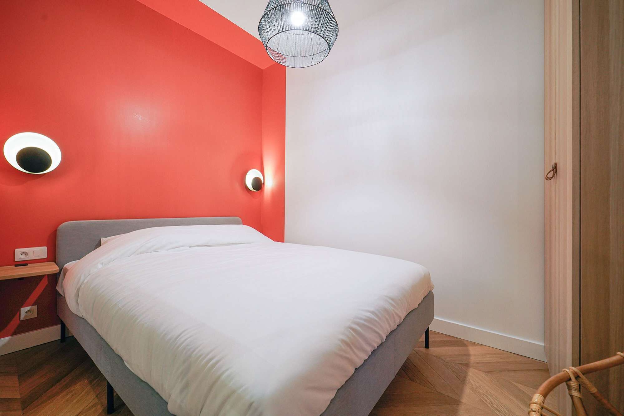 Une chambre à coucher avec un lit, une table de chevet, un mur rouge et un plancher en bois.