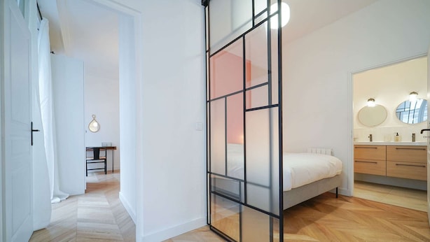 Une chambre à coucher comprenant un lit, une table de chevet et un miroir, ainsi qu’une salle de bain avec un lavabo et un miroir.