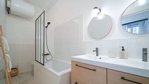 Une salle de bain moderne équipée d’une baignoire, d’une douche, d’un meuble-lavabo avec un miroir et d’un porte-serviettes.