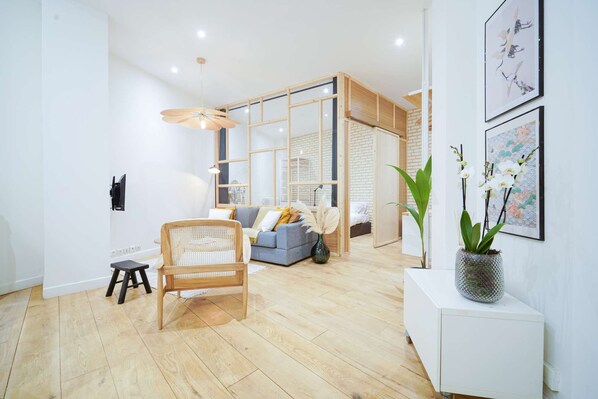 A modern living room with a wooden floor, a grey sofa, a wooden chair, and a white cabinet with a potted orchid.