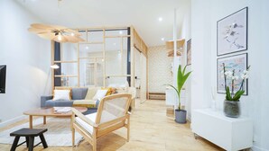 A modern living room with a wooden floor, a sofa, a coffee table, a chair, and a ceiling fan. There are framed pictures on the wall and a potted plant on a side table.