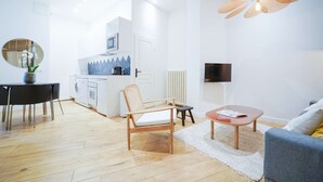 A modern living room with a sofa, a coffee table, a dining table with chairs, a kitchen area, and a TV mounted on the wall.