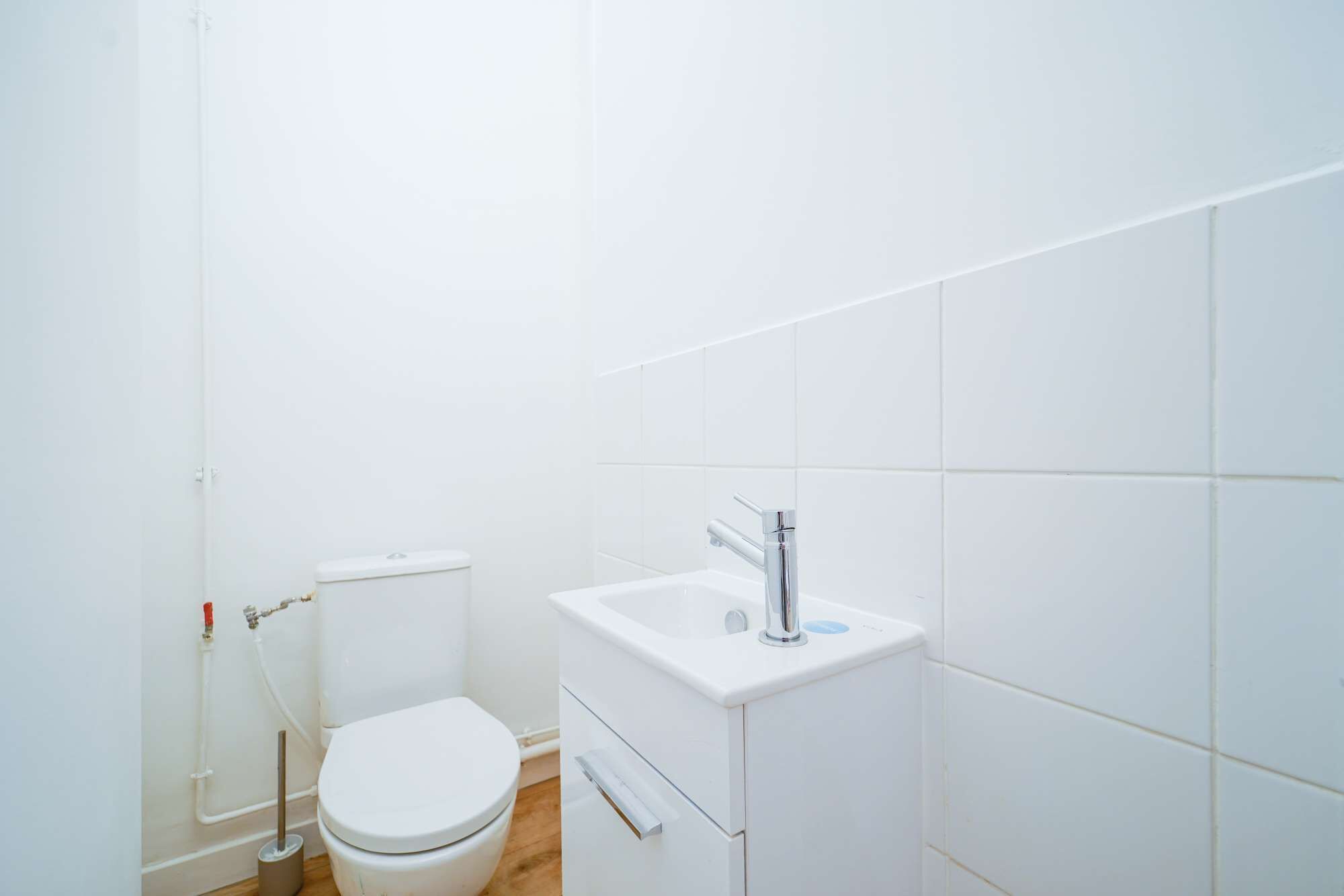 Une petite salle de bain blanche, équipée de toilettes, d’un lavabo et d’une douche.