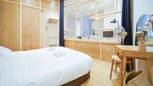 A modern hotel room with a large bed, a wooden desk, and a view through a glass partition.