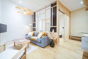 A modern living room with a grey sofa, wooden floor, and a large window with a view of a brick wall.