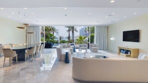 Een moderne woonkamer met een eethoek, grote ramen en uitzicht op palmbomen en gebouwen.