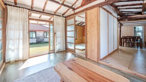 A spacious room with a wooden floor, a large sliding door leading to an outdoor area, and a dining table with chairs. - Jeju Motungedoljib Dogchaepension (Jeju City)