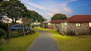 A stone building with a red-tiled roof, a gravel path leading to it, and a parked car. - Jeju Motungedoljib Dogchaepension (Jeju City)