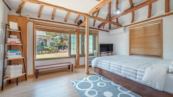 Un dormitorio con techo de madera, una cama con cubrecama a rayas, una estantería, un televisor y una ventana con persianas.