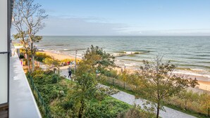 Uitzicht op de kust vanaf een hoog punt, met daaronder een zandstrand, een promenade met bomen en een voetpad.