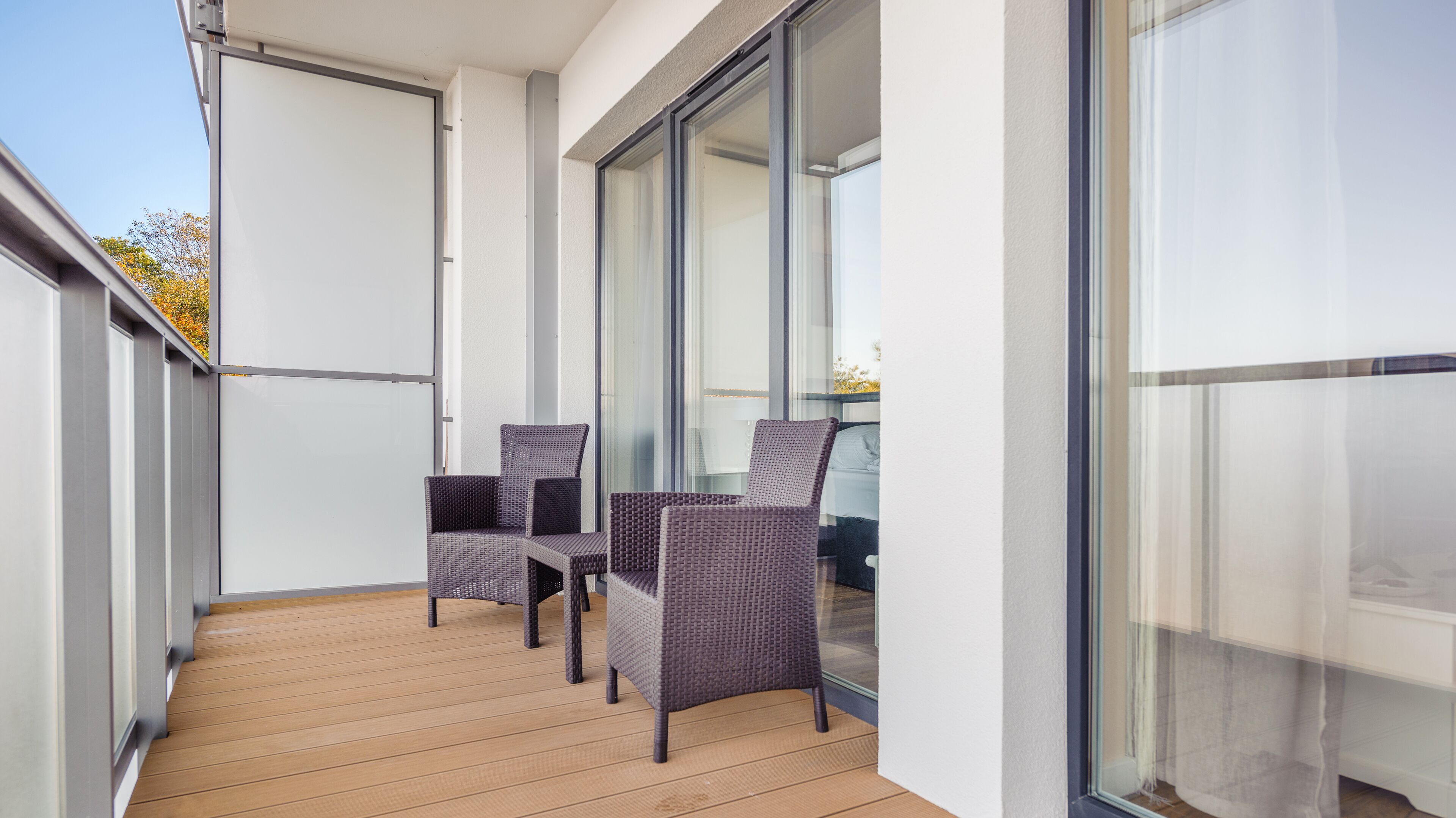 A balcony with two wicker chairs and a glass door leading to a room.