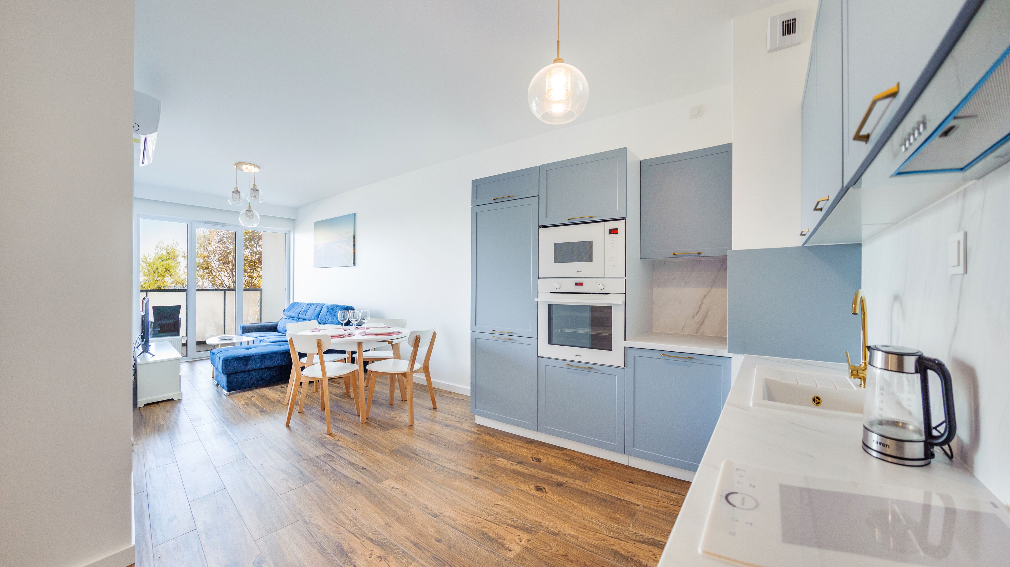 Una cocina moderna con electrodomésticos integrados, una zona de comedor con sofá azul y suelo de madera.
