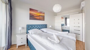 Quarto com cama, mesas de cabeceira, cômoda e uma pintura de um pôr do sol.