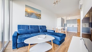 Een moderne woonkamer met een blauwe bank, een witte salontafel en een schilderij van een zonsondergang boven een pier.