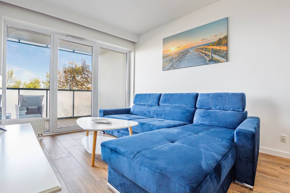 Ein modernes Wohnzimmer mit einem blauen Sofa, einem weißen Couchtisch und einem Fernseher auf einem weißen Schrank.