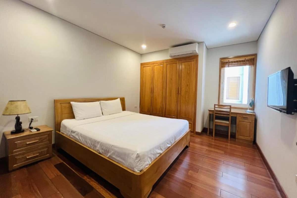 A bedroom with a wooden bed, a desk, a chair, and a TV.