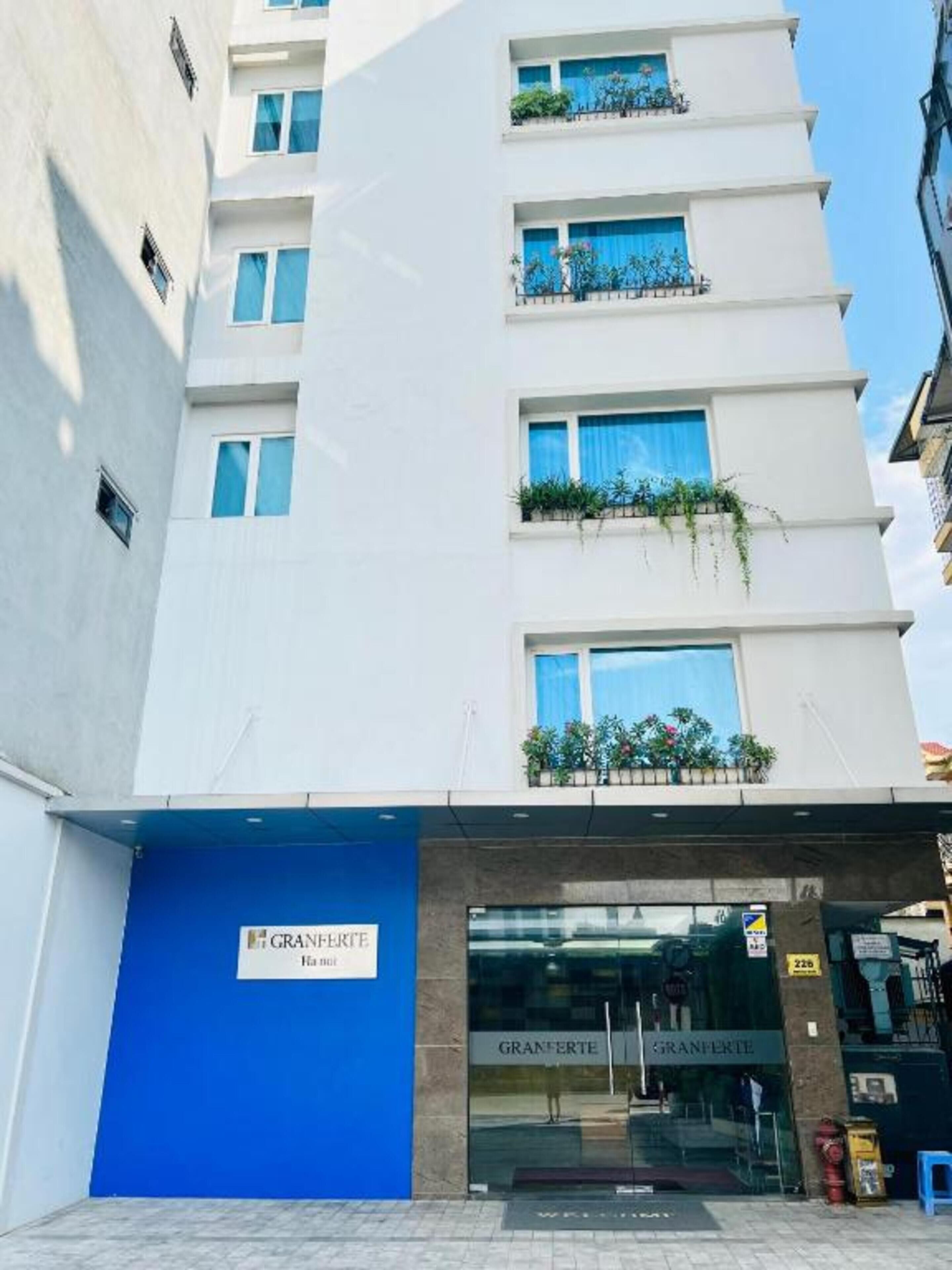 Un hotel a più piani con un ingresso blu e balconi adornati da piante.