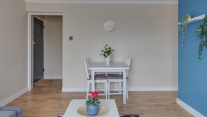 A dining area with a white table and chairs, a clock on the wall, and a potted plant. - BookedUK - Bright flat in Harlow (Harlow)